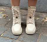 White combat boots on a person standing on a stone pavement.